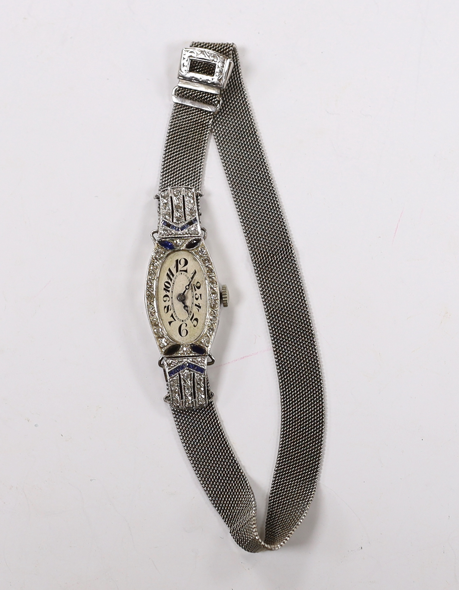 A mid 20th century white metal, sapphire and diamond cluster set Invicta Manufacturing Co. manual wind cocktail watch, on an adjustable 18ct white metal mesh bracelet, with oval Roman dial